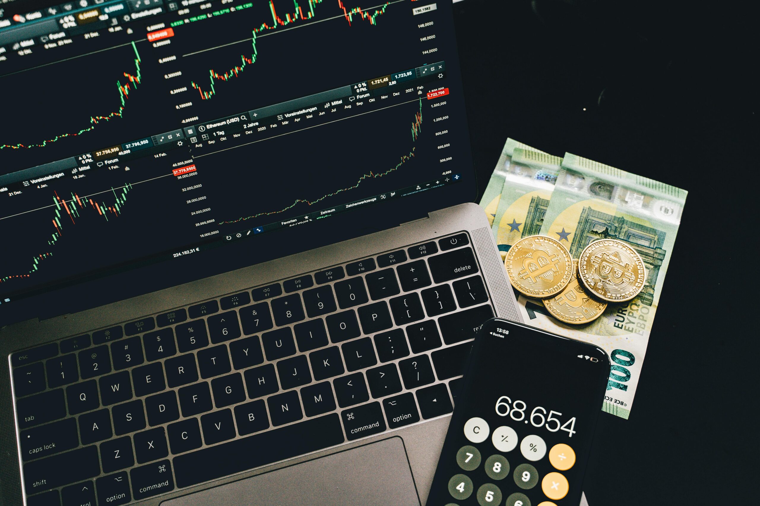 Laptop con gráficos de trading, calculadora y billetes de euro con monedas de criptomonedas, categoría Finanzas e Inversión