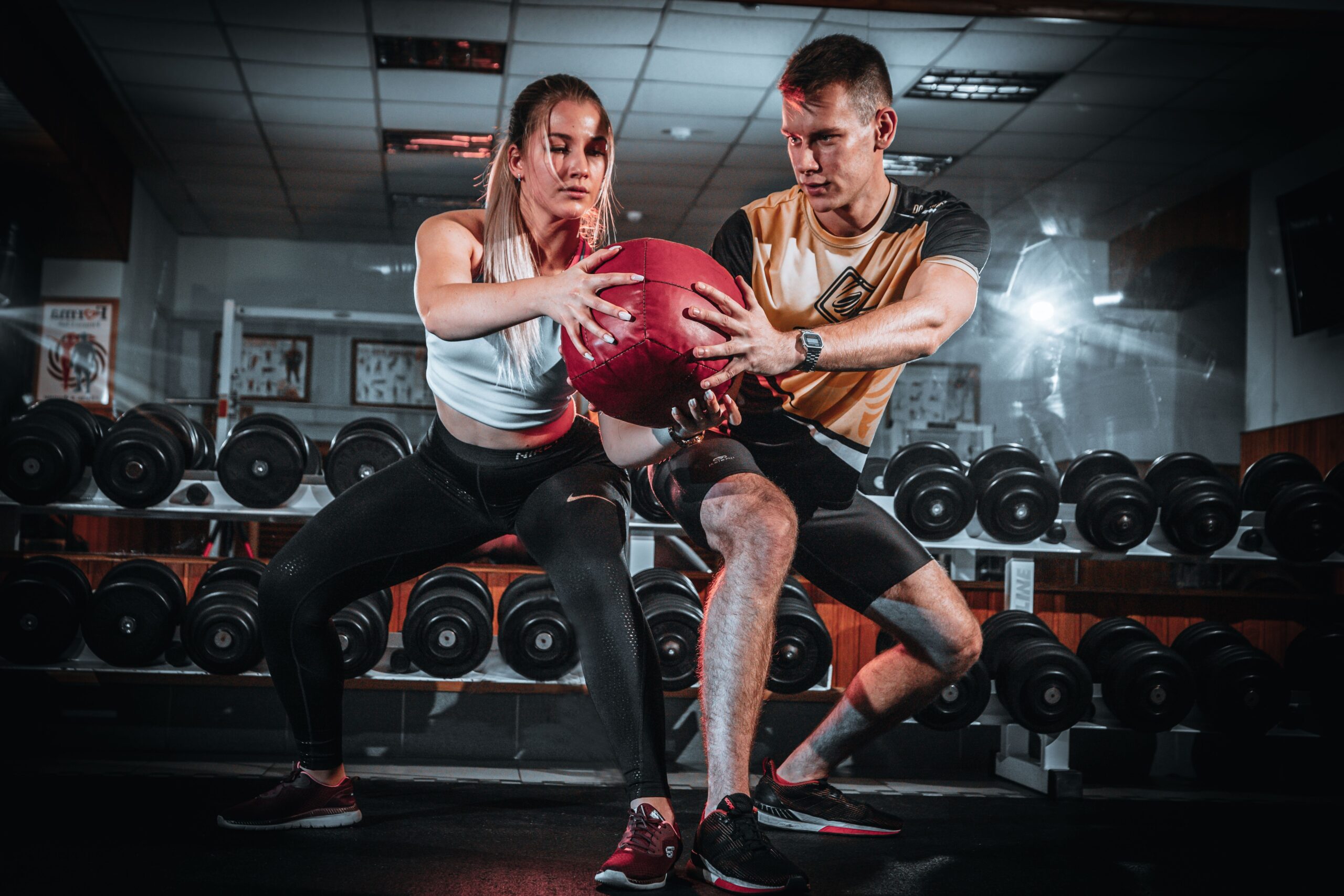 Entrenador y alumna haciendo ejercicio con balón medicinal en el gimnasio, categoría Salud y Deportes