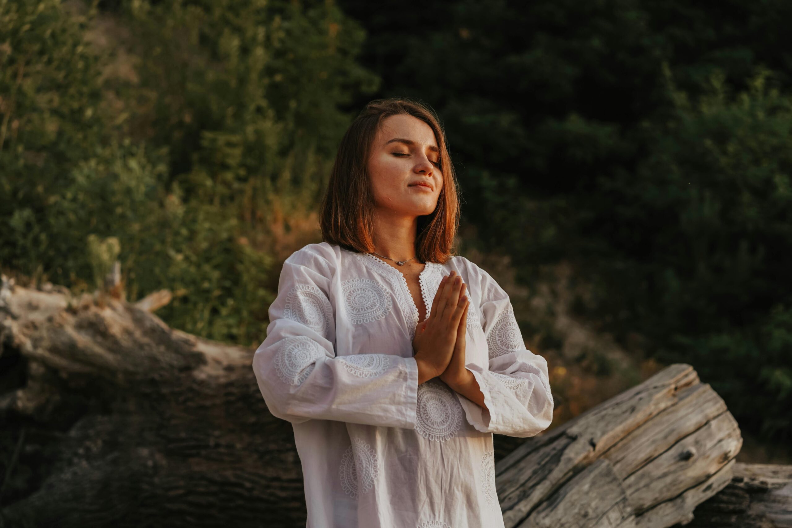 Mujer meditando al aire libre con manos en posición de oración, categoría Bienestar y Mindfulness