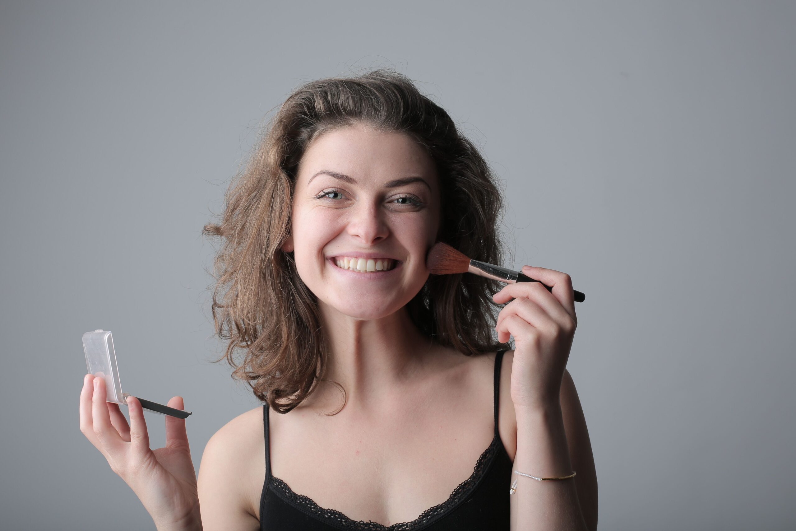 Mujer sonriente aplicándose maquillaje con brocha, categoría Belleza y Maquillaje